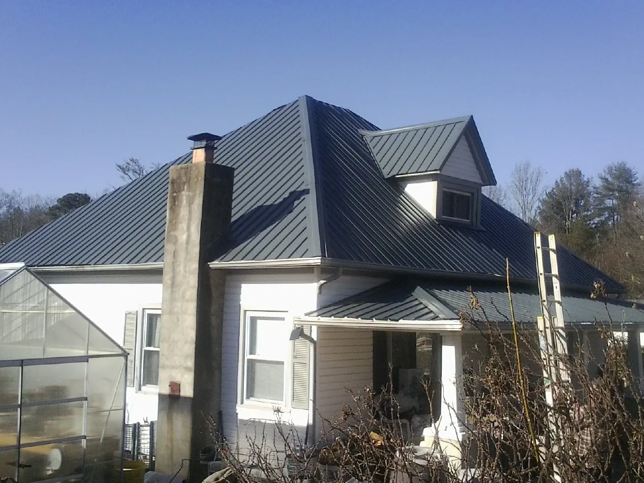 Dark blue standing seam metal roof on a white farmhouse with dormer — Slate & Tile Roof Repair by Roofing Brothers in North Rose