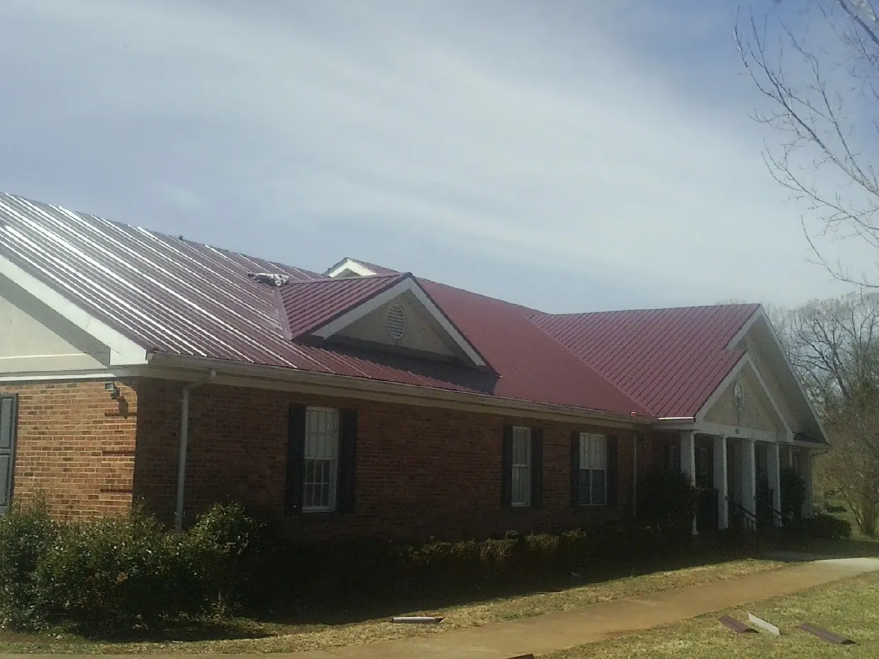 Red metal roof with gabled entries on a long brick building, from a Hail Damage Roof Repair job in North Rose