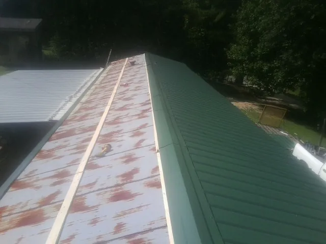 Old rusted panels beside newly installed green metal roofing — Wind Damage Roof Repair by Roofing Brothers in North Rose
