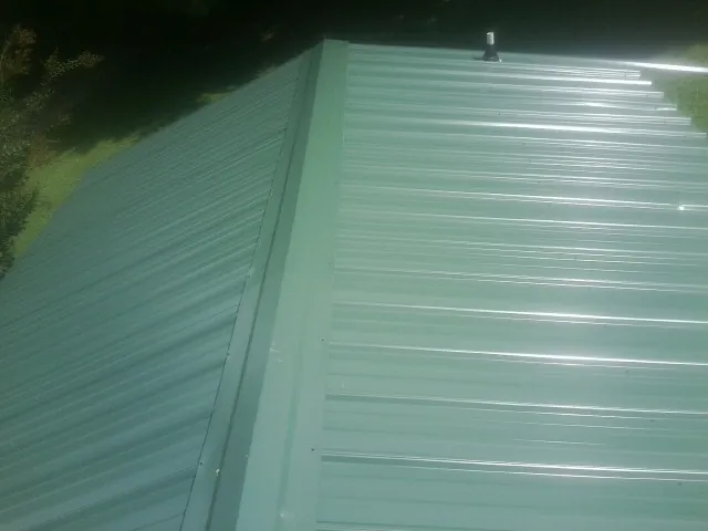 New green metal panels meeting at the ridge of a roof — Flat Roof Repair work by our crew in North Rose
