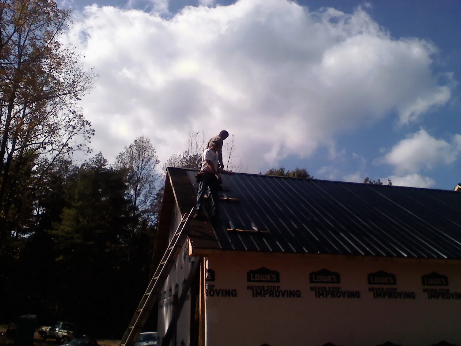 Roofer fastening dark metal panels high against a cloudy sky, from a Roof Inspection job in North Rose