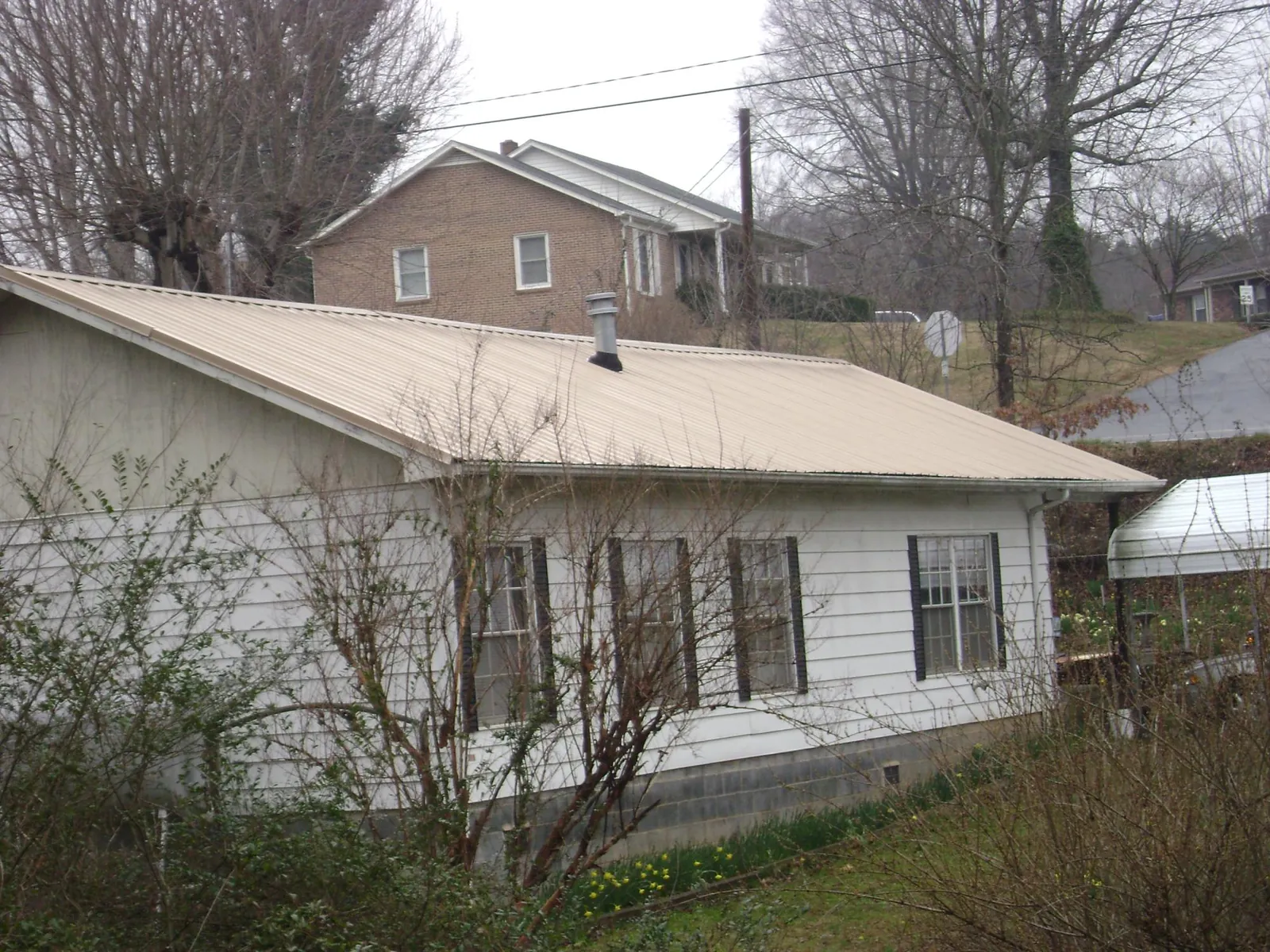 Tan metal roof on a white sided house set into a hillside — Commercial Roofing by Roofing Brothers in North Rose