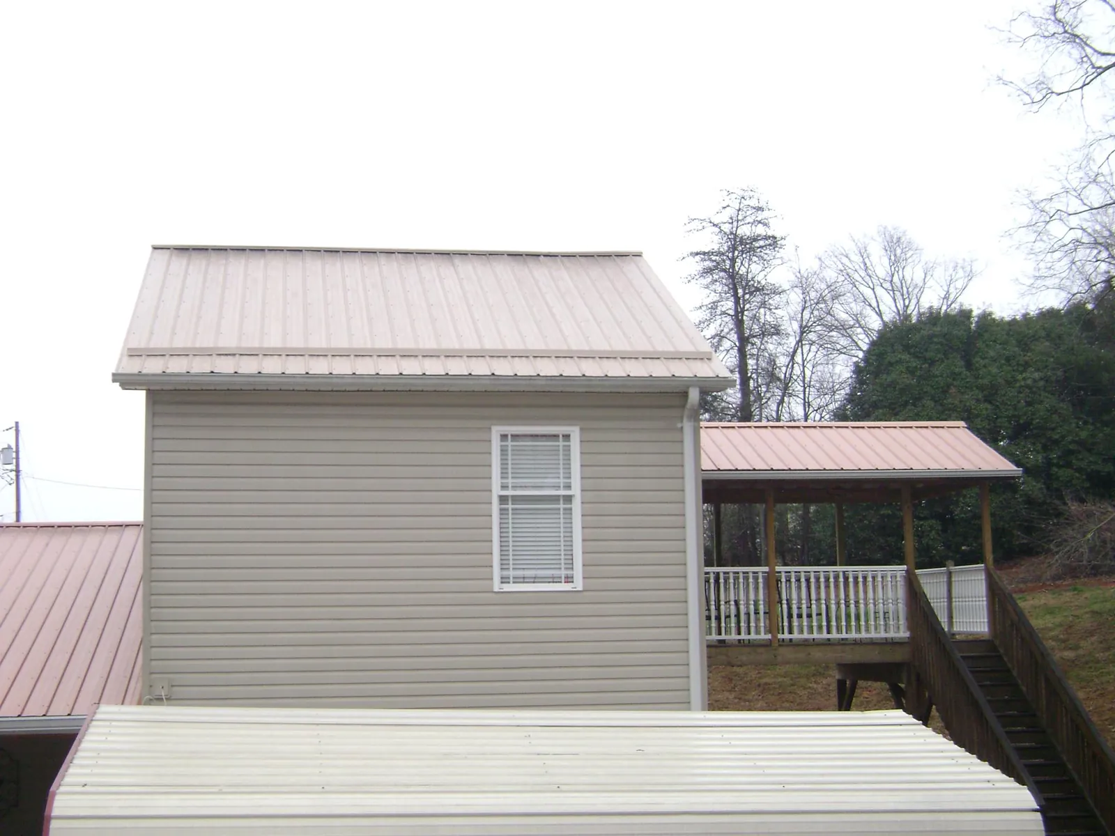 Tan metal roofs on a two story addition and attached porch, from a Roof Replacement job in North Rose